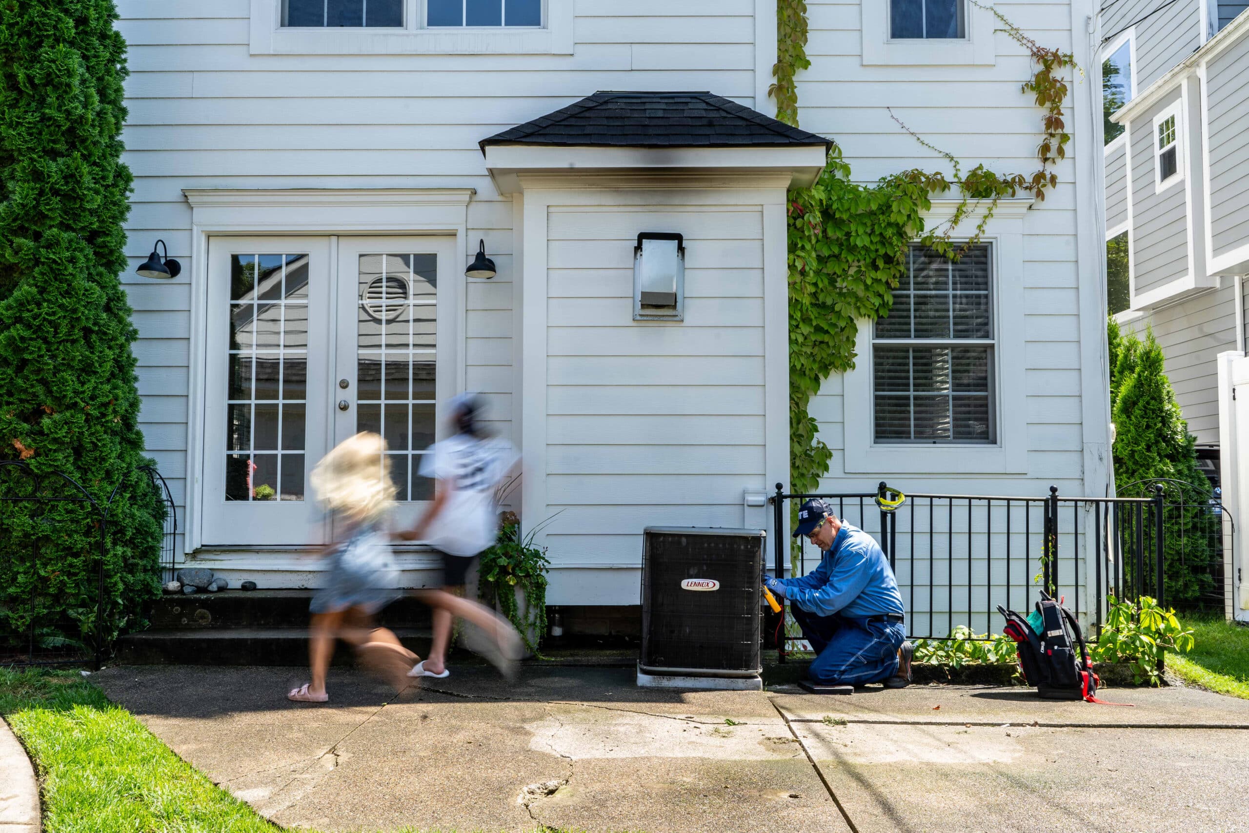Happy family outside a charming home during summer with kids playing and a repair worker nearby.